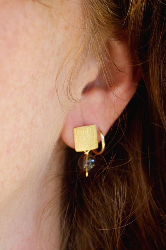 Close-up of a gold earring worn by a person with brown hair.