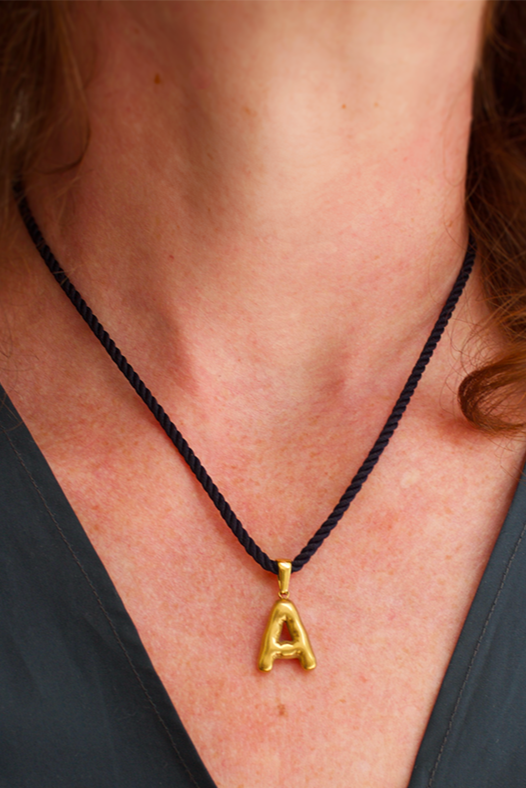 Gold necklace with a 'A' pendant on a person wearing a dark top.