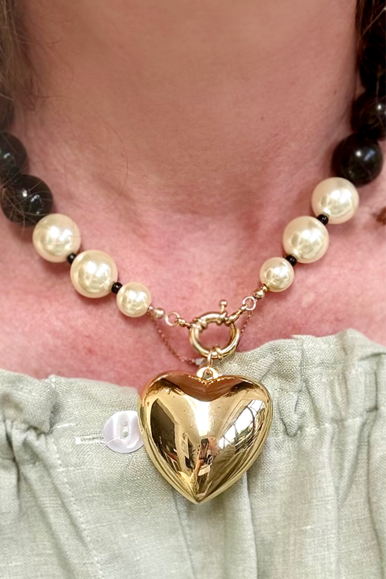 Necklace with heart-shaped pendant and black and white beads on a person wearing a light green top.