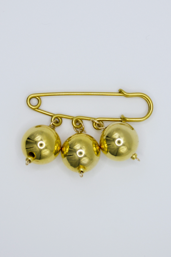 Gold brooch with three round embellishments on a light gray background