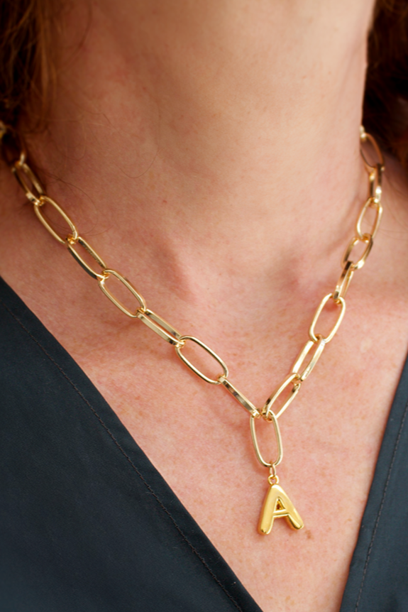 Gold chain necklace with a letter 'A' pendant on a person wearing a dark blue top.