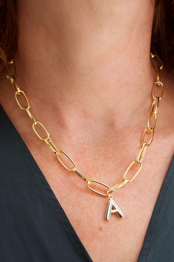 Gold chain necklace with a letter 'A' pendant on a person wearing a dark blue top.