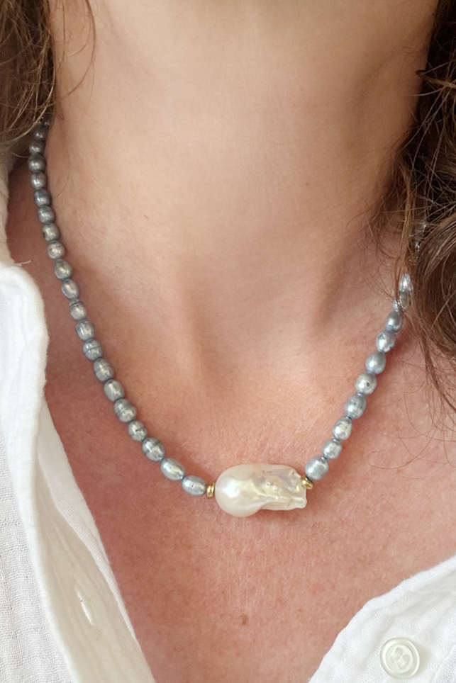 Pearl necklace with a large central bead worn by a person in a white shirt.