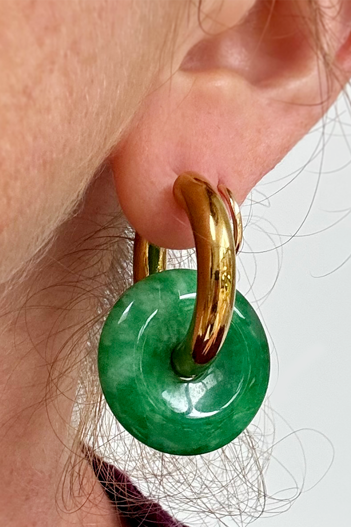 Gold hoop earring with a green jade-like stone worn by a person.