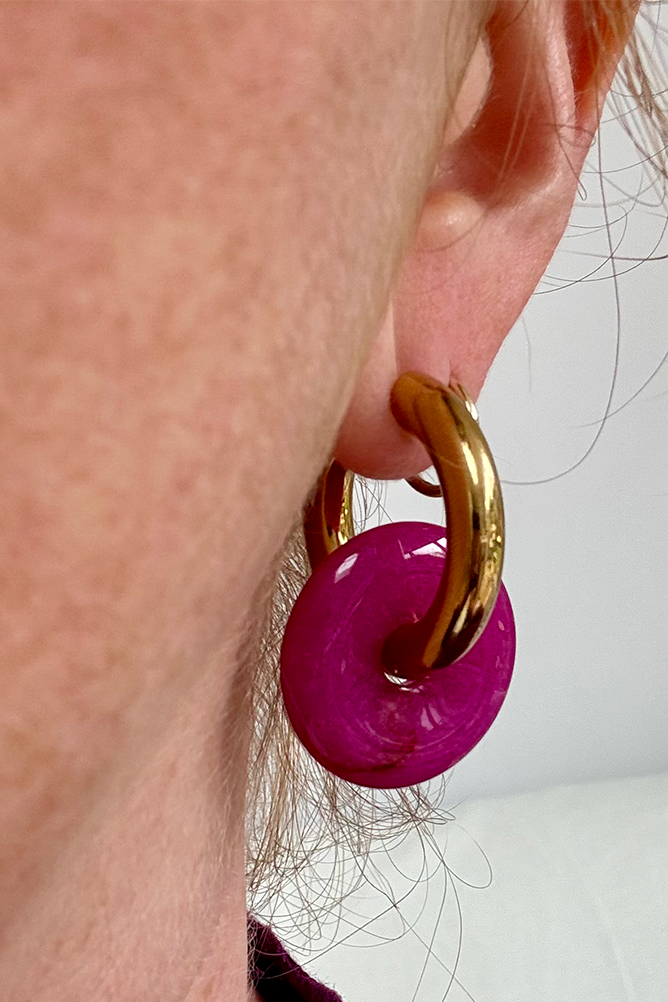 Close-up of a pink earring with gold hoop worn by a person.