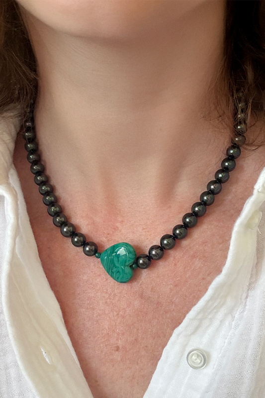 Necklace with black beads and a green heart-shaped pendant worn by a person in a white shirt.