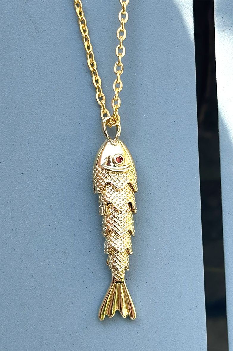 Gold fish-shaped pendant on a chain against a blue background