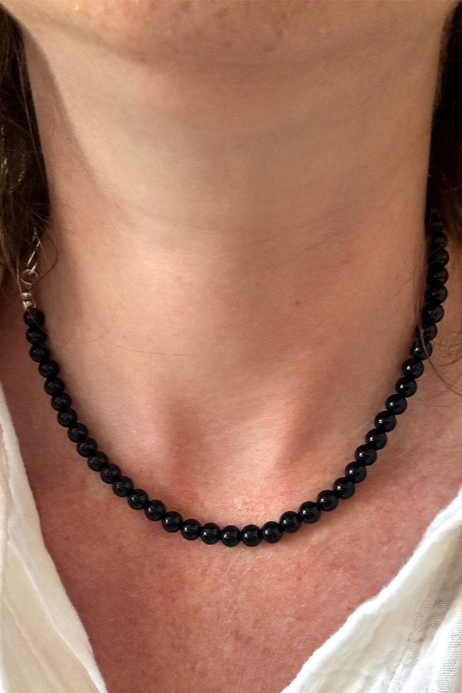 Person wearing a black beaded necklace with a white shirt