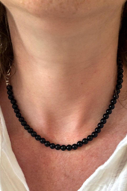 Person wearing a black beaded necklace with a white shirt