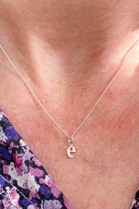 Necklace with a letter 'e' pendant worn by a person in a floral shirt.