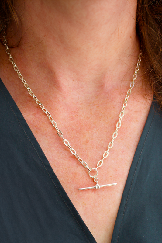 Gold chain necklace with a small pendant worn by a person against a dark background