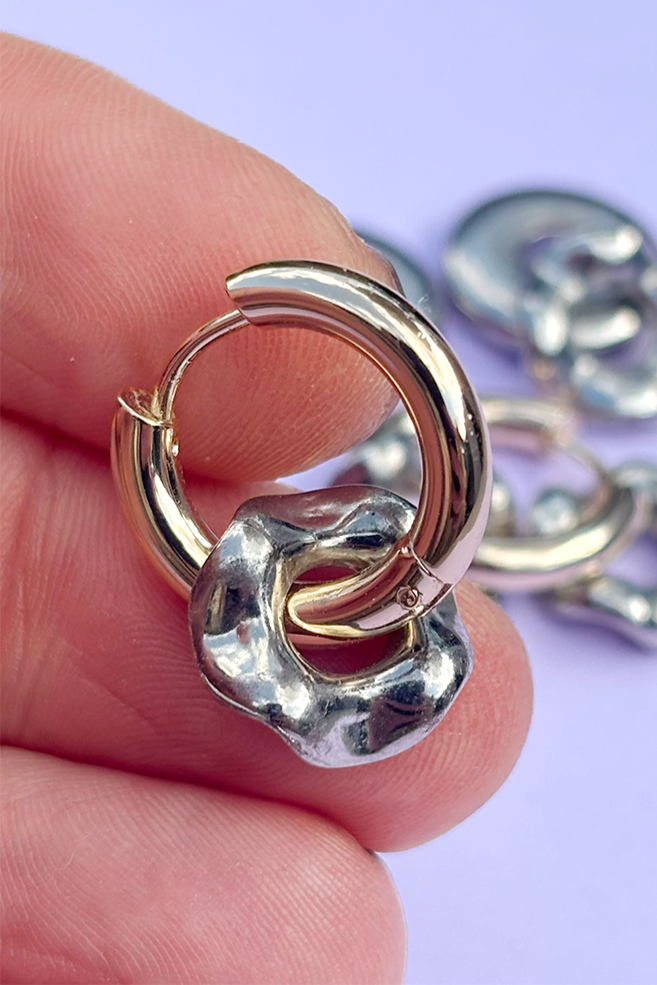 Gold and silver hoop earrings held between fingers with a light purple background