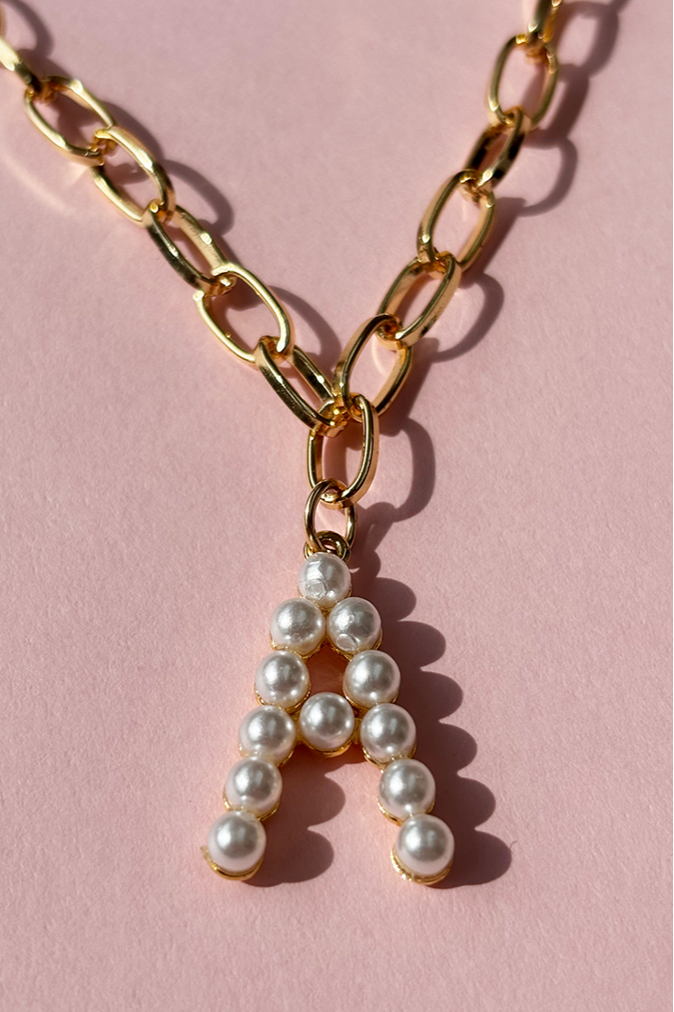 Gold chain necklace with a pearl 'A' pendant on a pink background