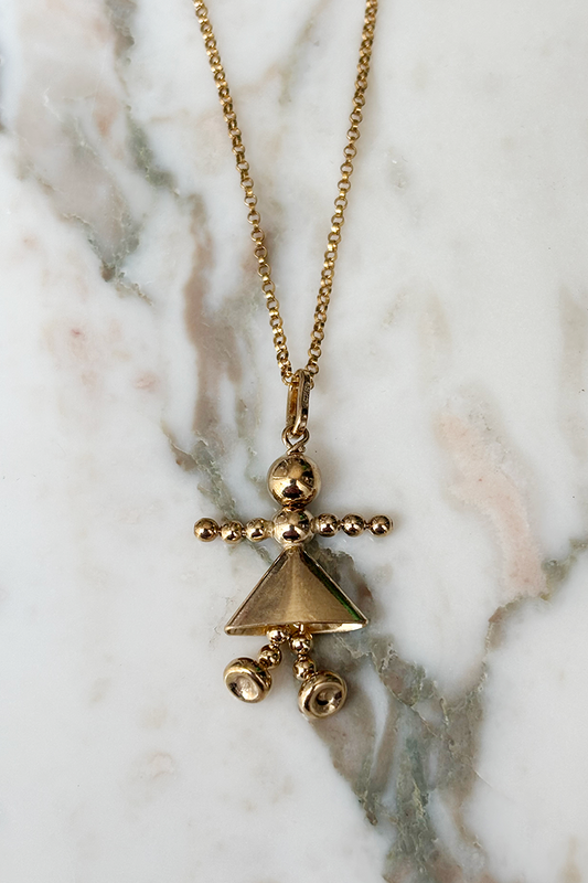 A gold necklace with a doll-shaped pendant, displayed on a white and gray marble surface.